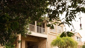 A two-story house with a balcony, brick exterior, and potted plants. - Charming 4-bedroom Apartment in Jeffreys Bay, South Africa (Jeffreys Bay)