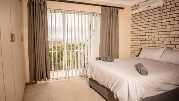 A bedroom with a bed, curtains, a balcony, and a brick wall.