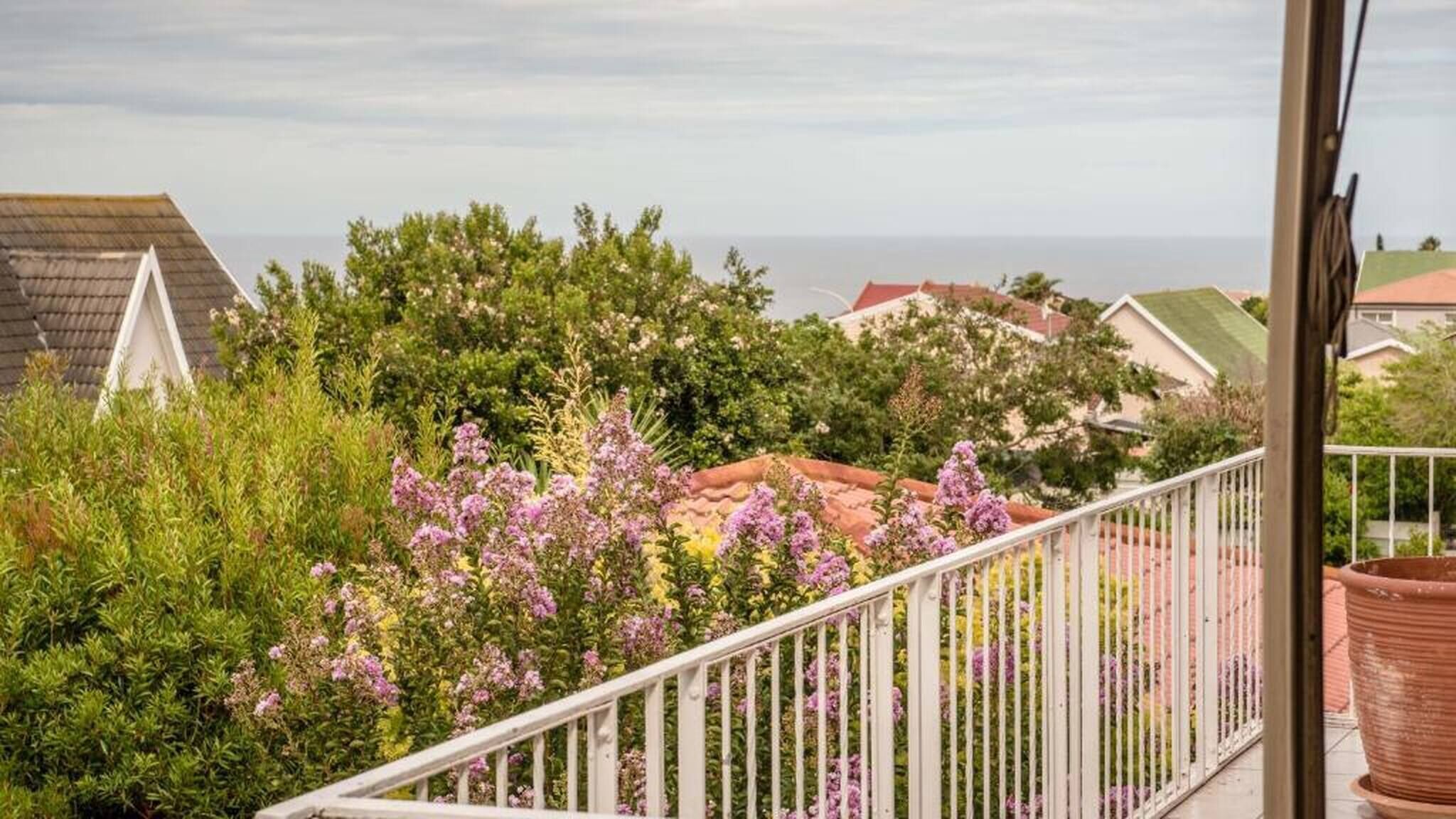 Een balkon met een hekwerk, met uitzicht op een woonwijk met huizen en een helder uitzicht op zee.