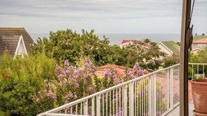 A balcony with a railing overlooking a residential area with houses and a clear view of the sea. - Charming 4-bedroom Apartment in Jeffreys Bay, South Africa (Jeffreys Bay)