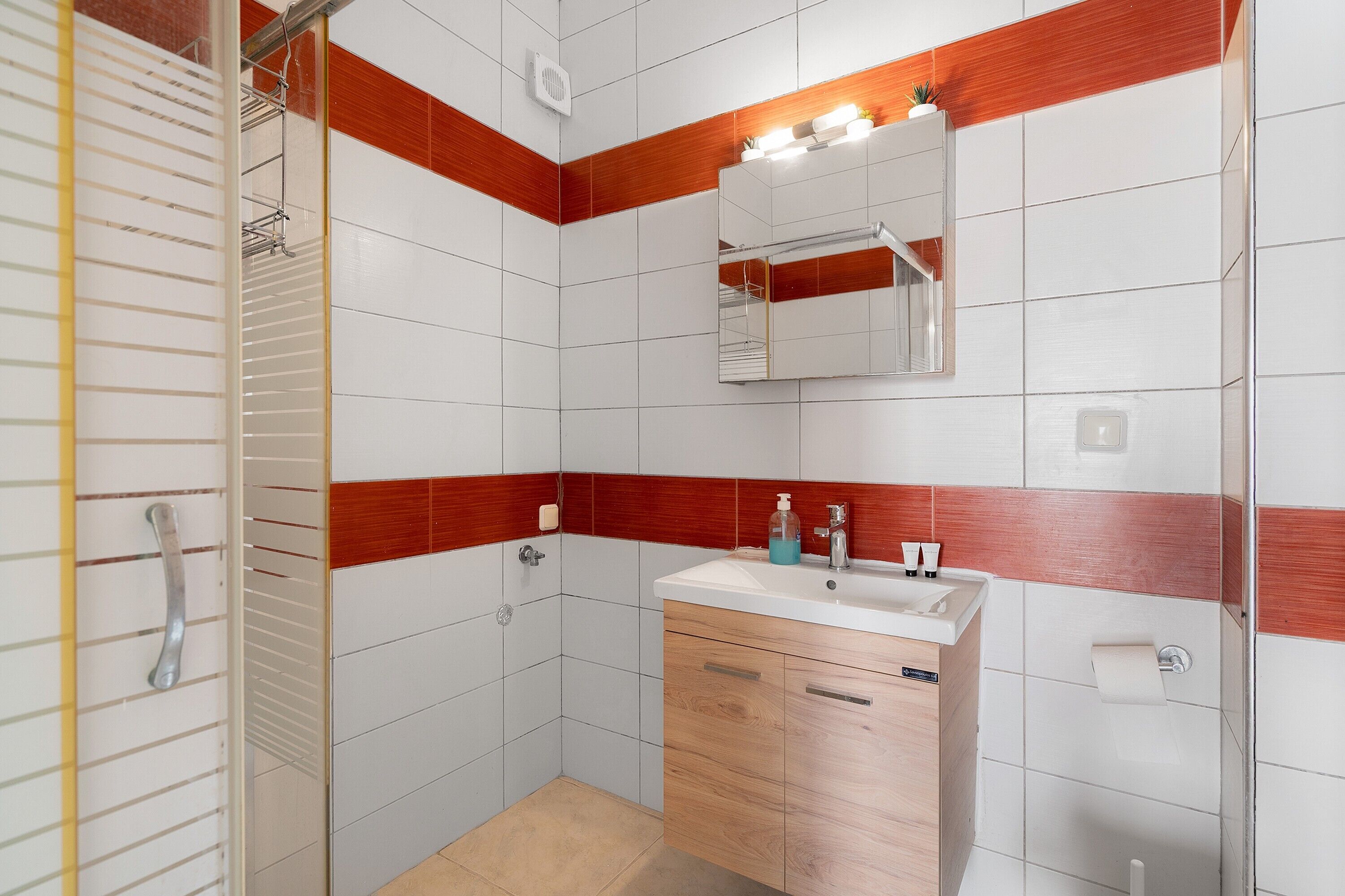 Un bagno con piastrelle bianche e rosse, un mobiletto in legno, un lavandino con specchio e uno spazio doccia.