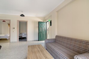 Ein Zimmer mit einem grauen Sofa mit Karomuster, einem Bett mit weißer Bettwäsche, einer grünen Tür und einem kleinen Tisch.