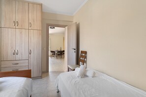 A hotel room with two beds, a wooden wardrobe, a dining area, and a bathroom.