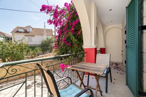 A balcony with a table and chairs, surrounded by a railing and a view of a house with a tiled roof.