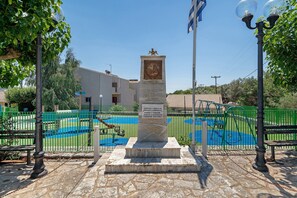 A monument with inscriptions, surrounded by a playground with a green fence, and a building in the background. - Appartment 'By The Sea 3' with Private Garden (Meganisi)