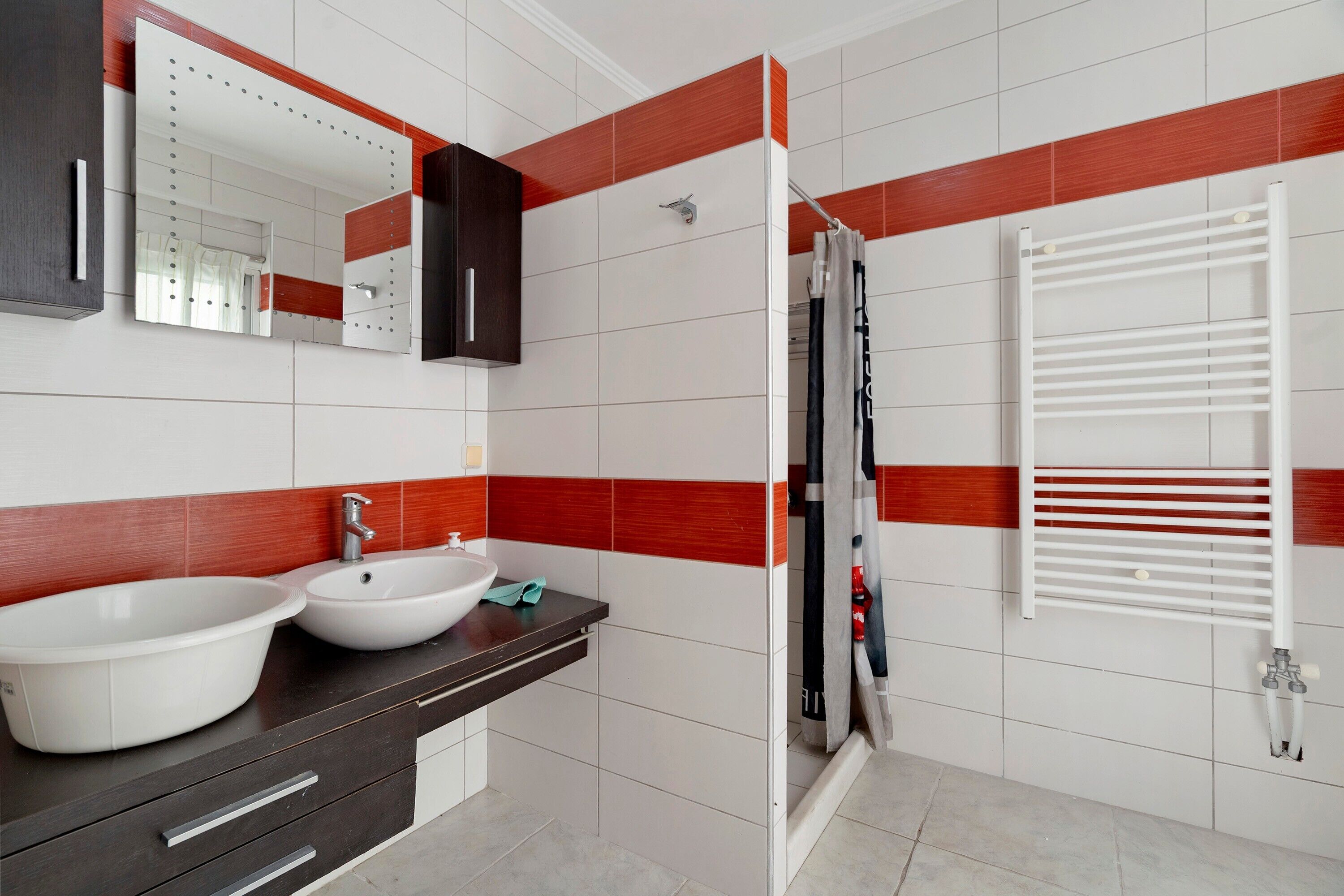 A modern bathroom with a double sink vanity, a mirror, a towel rack, and a shower with a white towel rack.