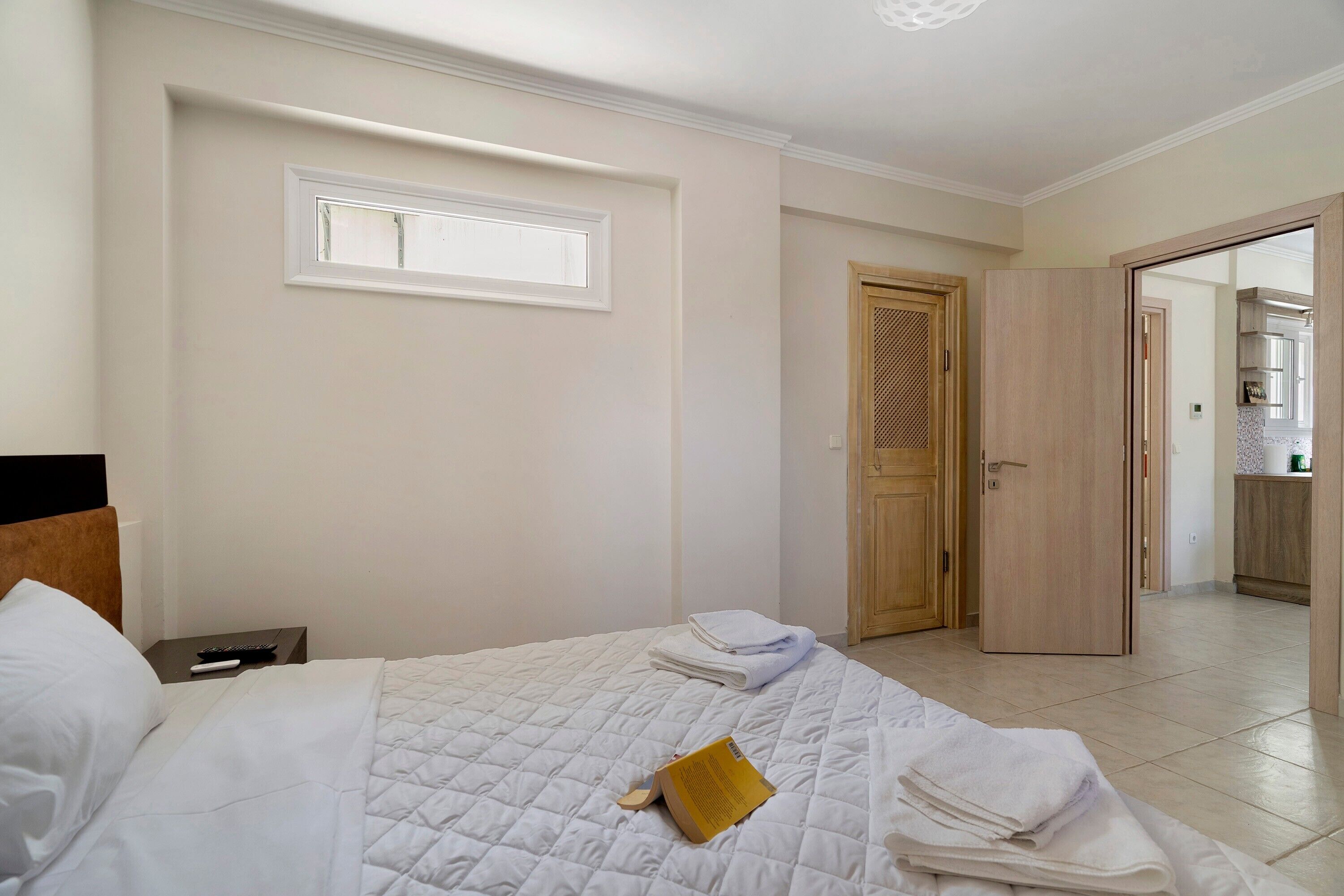 A hotel room with a bed, a window, a door, and a view into the kitchen.