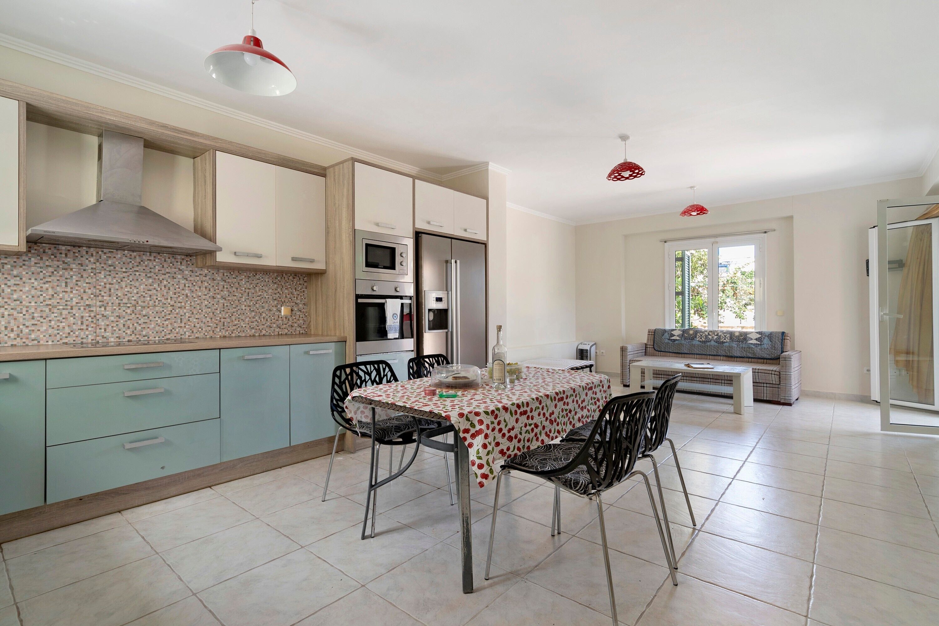 A modern kitchen with a dining area, featuring a table with chairs, a sofa, and a glass door leading outside.