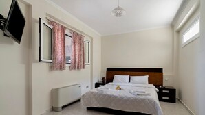 Habitació d'hotel amb un llit, una taula de nit, una làmpada, un radiador, un televisor penjat a la paret i una finestra amb cortines.