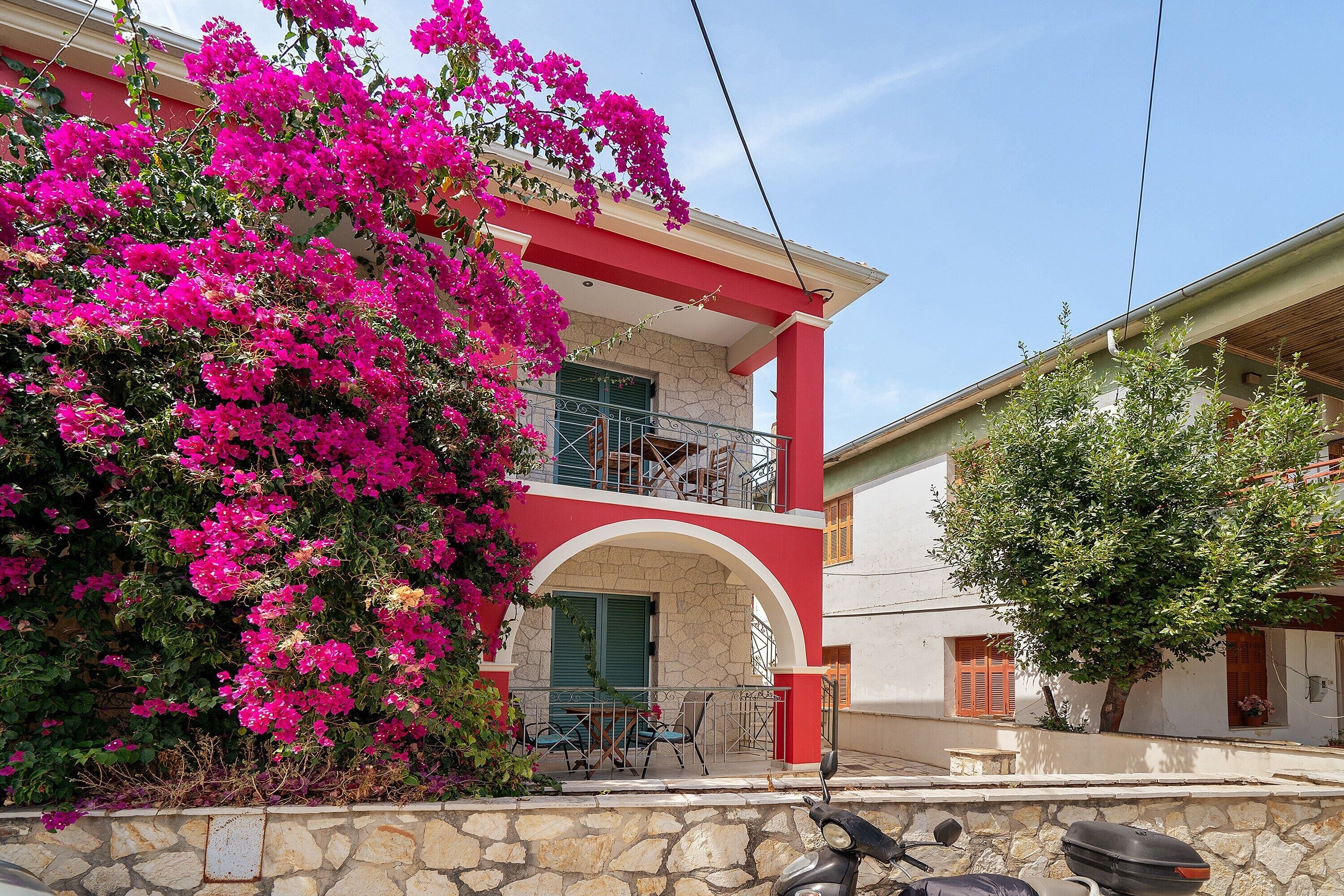 A two-story building with a balcony, a stone wall, and a scooter parked in front.
