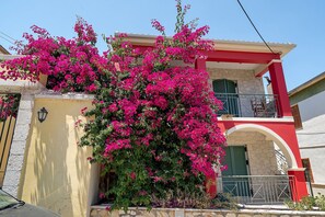 A building with a balcony and a vibrant bougainvillea plant. - Appartment 'By The Sea 3' with Private Garden (Meganisi)