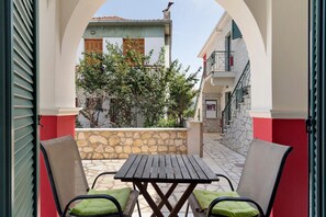 An outdoor seating area with a table and chairs, a stone wall, and a view of a building with a balcony. - Appartment 'By The Sea 3' with Private Garden (Meganisi)