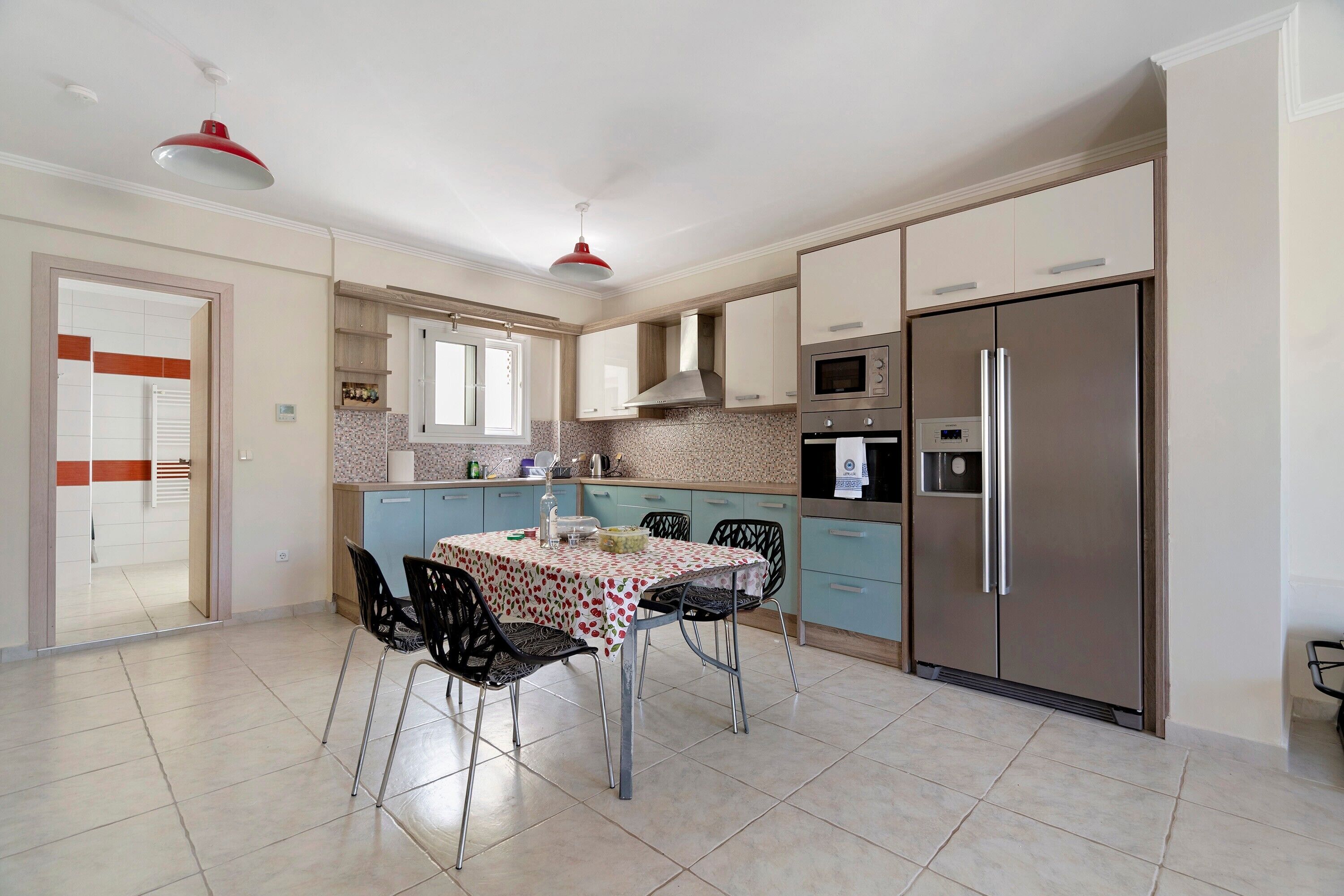 A modern kitchen with a dining area, featuring a refrigerator, oven, microwave, and a table with chairs.
