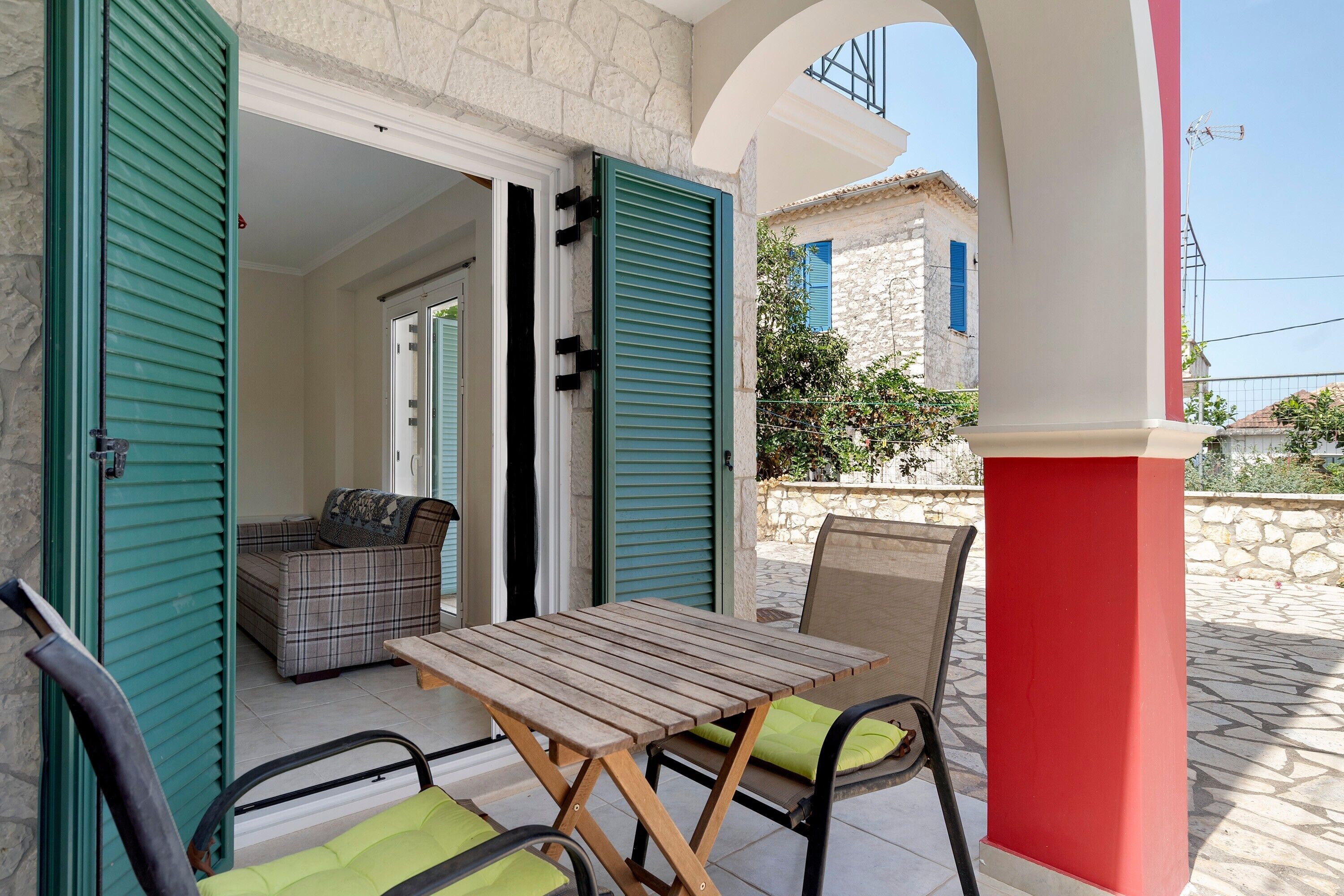 An outdoor seating area with a table and chairs, a sofa, and a partially open door leading to a room.