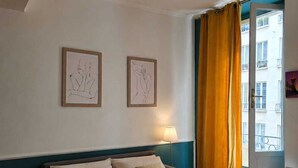 A bedroom with a bed, a nightstand, a lamp, and two framed artworks on the wall. - CHICKY HOUSE (Paris)