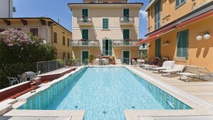 Ein rechteckiger Swimmingpool mit gefliestem Sonnendeck, umgeben von Gebäuden mit Balkonen und Fenstern.
