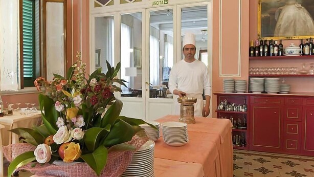 Ein Essbereich mit gedecktem Tisch, ein Koch in Uniform und eine Küche im Hintergrund.
