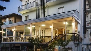 A two-story building with balconies, a ground-floor restaurant with outdoor seating, and a staircase leading to the upper floor.
