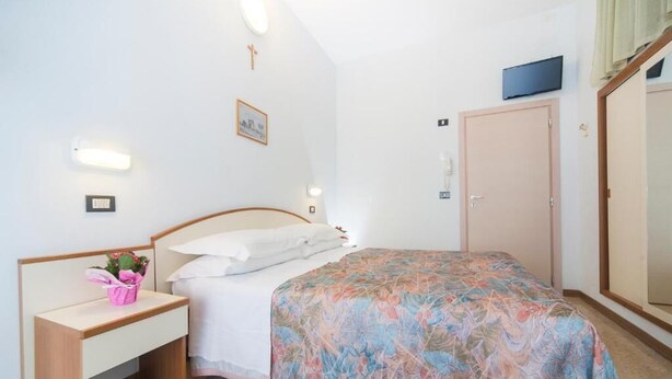 A bedroom with a bed, bedside table, and a television mounted on the wall.