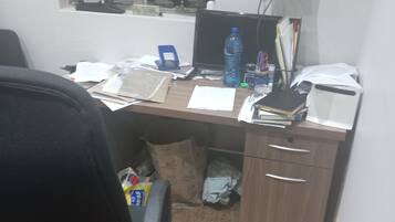 Ein unordentlicher Büroarbeitsplatz mit Schreibtisch, Stuhl, Computer und verschiedenen Büromaterialien.