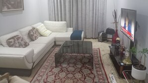 A living room with a white sofa, a glass coffee table, a patterned rug, a television, and a potted plant. - Luxurious 4-bedroom House Rental With Pool Access in Ngaka Modiri Molema (Mahikeng)