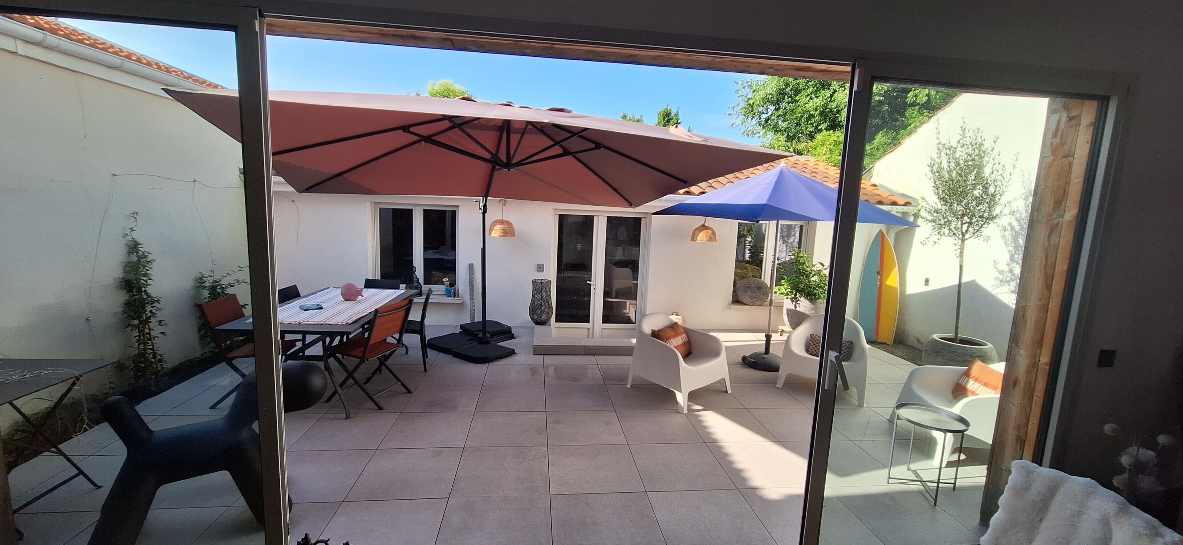 A patio area with a table and chairs, a large umbrella, and a sliding glass door leading to a garden.