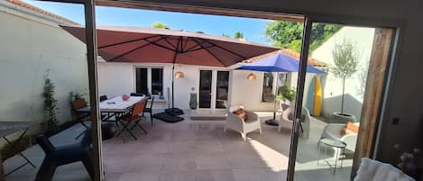 A patio area with a table and chairs, a large umbrella, and a sliding glass door leading to a garden.