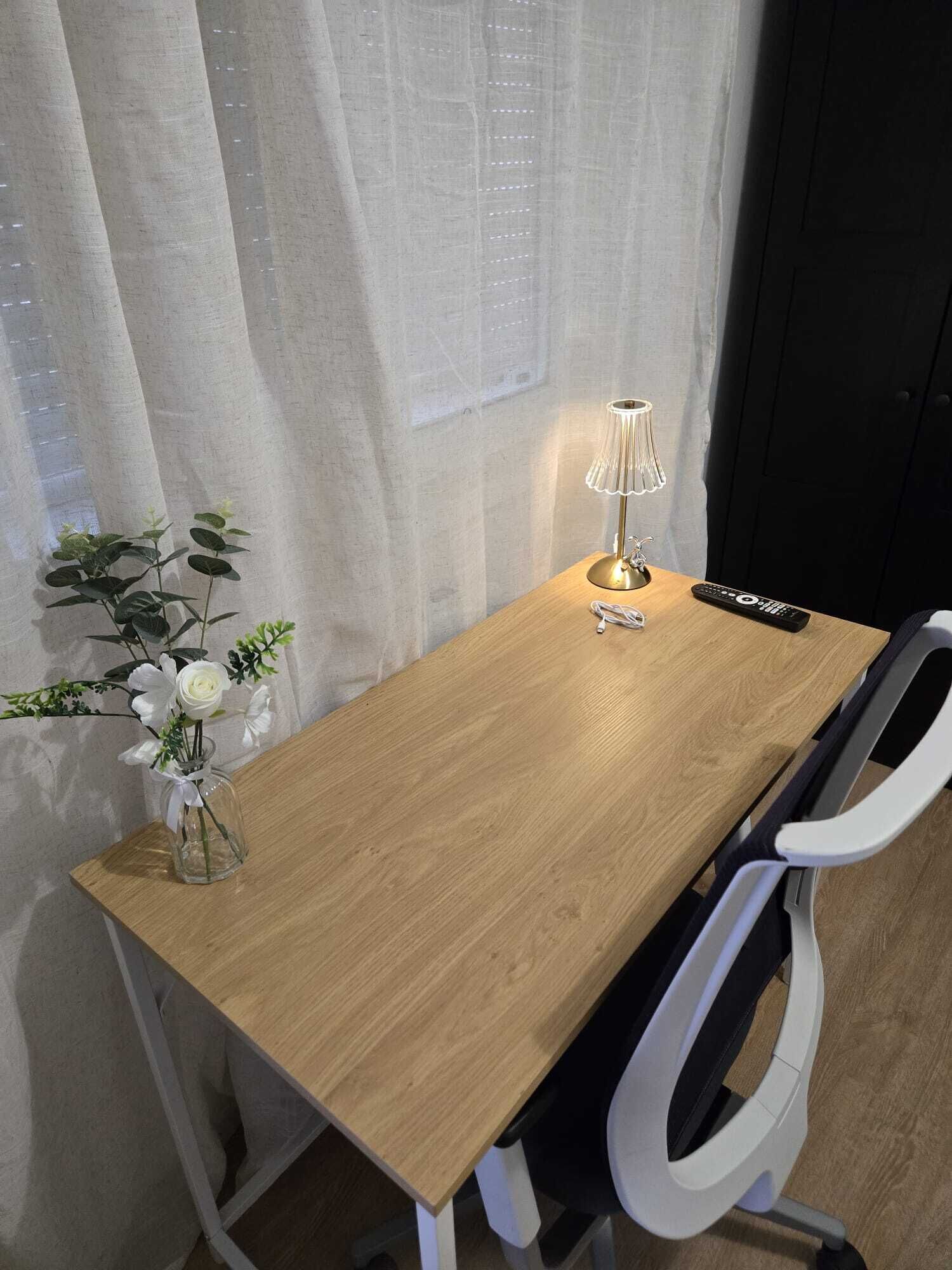 Une table en bois, une lampe, une télécommande et un vase avec des fleurs.