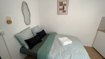 Ein Schlafzimmer mit einem Bett, Kissen, einem Nachttisch, einem Spiegel und einem gerahmten Bild an der Wand.