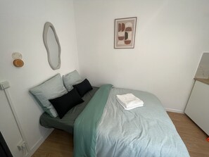 Un dormitorio con cama, almohadas, una mesita de noche, un espejo y un cuadro en la pared.