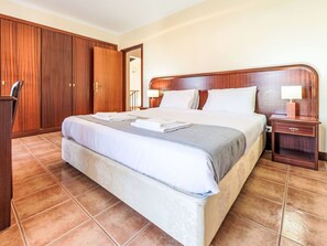 A hotel room with a large bed, wooden wardrobe, bedside table with lamp, and tiled floor. - Arrifes Porto Santo by Interhome (Porto Santo)