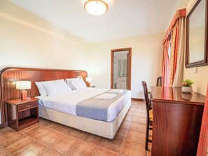 Ein Hotelzimmer mit einem Bett, Nachttischen, einem Schreibtisch, einem Sessel und einem Spiegel.