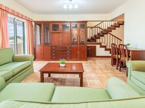 Ein Wohnzimmer mit einer Couch, einem Couchtisch mit Pflanze, einem Holzschrank und einer Treppe.