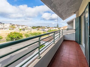 Ein Balkon mit Metallgeländer, Fliesenboden und Blick auf ein Wohngebiet mit Häusern und Grünflächen.