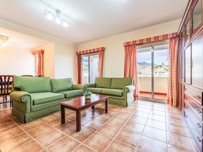 A living room with a sectional sofa, a coffee table, and a view through a sliding glass door. - Arrifes Porto Santo by Interhome (Porto Santo)