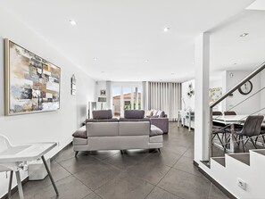 A modern living room with a sectional sofa, a dining area with a table and chairs, and a staircase leading to another level. - Florentina by Interhome (Gaula)