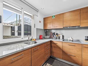 A modern kitchen with wooden cabinets, a stainless steel sink, and a window overlooking a building. - Florentina by Interhome (Gaula)
