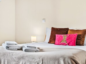 A neatly made bed with folded towels, a lamp, and two pillows on a plain wall. - Casa da Abegoaria by Interhome (Caniço (Madeira))
