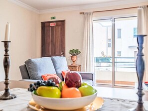 A room with a bed, a bowl of fruit, a potted plant, and a view of buildings through a window. - Casa da Abegoaria by Interhome (Caniço (Madeira))