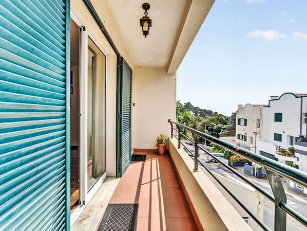 En balkon med udsigt til gaden, en potteplante og en dør med skydeliste.