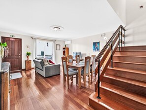 A modern living room with a staircase, wooden flooring, a sofa, dining table, and chairs. - Casa da Abegoaria by Interhome (Caniço (Madeira))