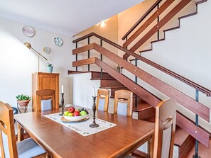 A dining area with a wooden table, chairs, and a fruit bowl. A staircase with wooden steps and metal railings is visible in the background. - Casa da Abegoaria by Interhome (Caniço (Madeira))