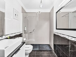 Et moderne badeværelse med en glasafskærmet brusebad, et hvidt toilet og et stort spejl.