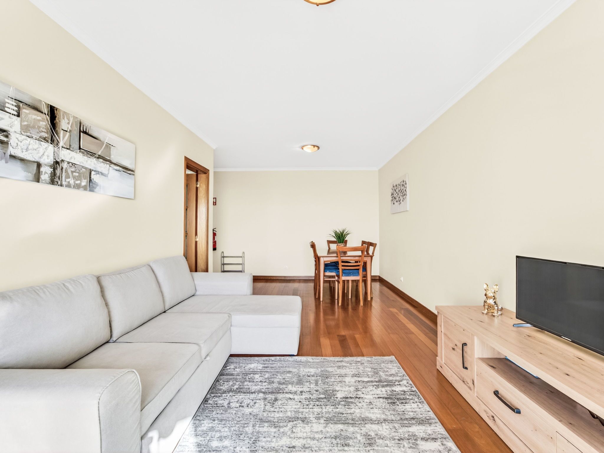 Ein modernes Wohnzimmer mit einer Couch, einem Fernseher, einem Holzkasten und einem Essbereich mit Stühlen und einem Tisch.
