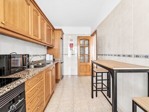A kitchen with wooden cabinets, a granite countertop, a black microwave, a coffee maker, and a wooden table. - Apartment Baly Formosa by Interhome (Funchal (Madeira))