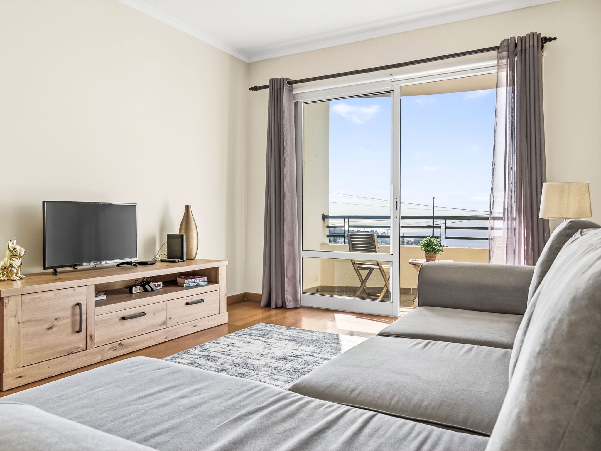 Een moderne woonkamer met een bank, televisie, houten kast en een balkon met uitzicht.