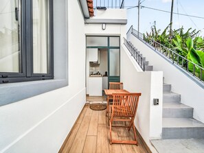 A modern kitchen with a wooden table and chairs, a staircase leading to an upper level, and a view of lush greenery. - Panoramic Studio View by Interhome (Funchal (Madeira))