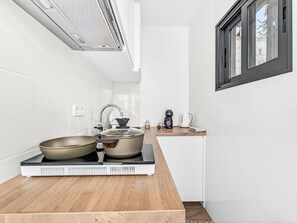 Una cuina moderna amb rajoles blanques, taulell de fusta, fogó i finestra.