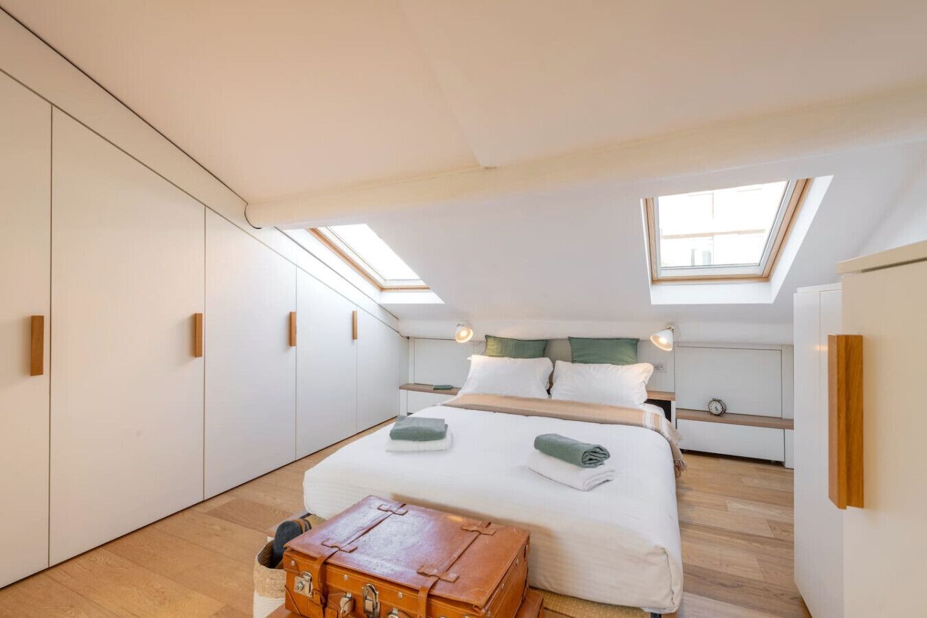 Una camera da letto con un lucernario, un letto con cuscini, un baule di legno e un piccolo tavolo.