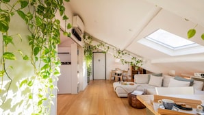 En moderne loftlejlighed med ovenlys, trægulv, sofa, spiseområde og grønne planter.
